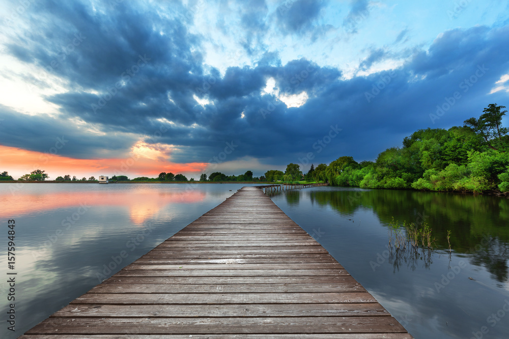 Wooden path bridge over lake at stormy sunset