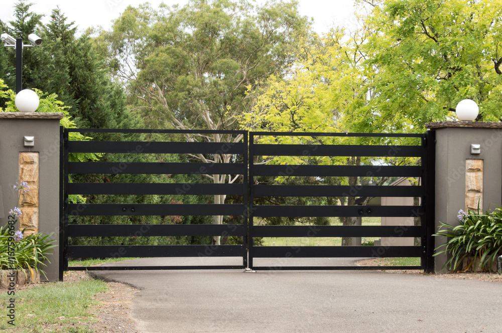 Black metal driveway entrance gates set in brick fence Black metal driveway entrance gates set in brick fence