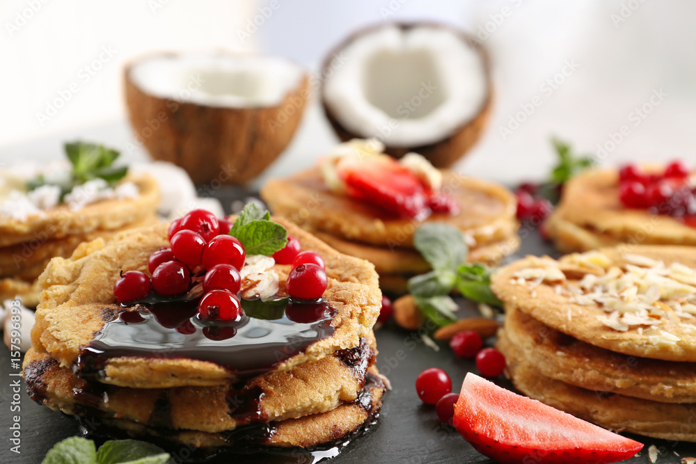 Stacks of delicious coconut pancakes with sweet sauce, berries and mint on slate plate, close up