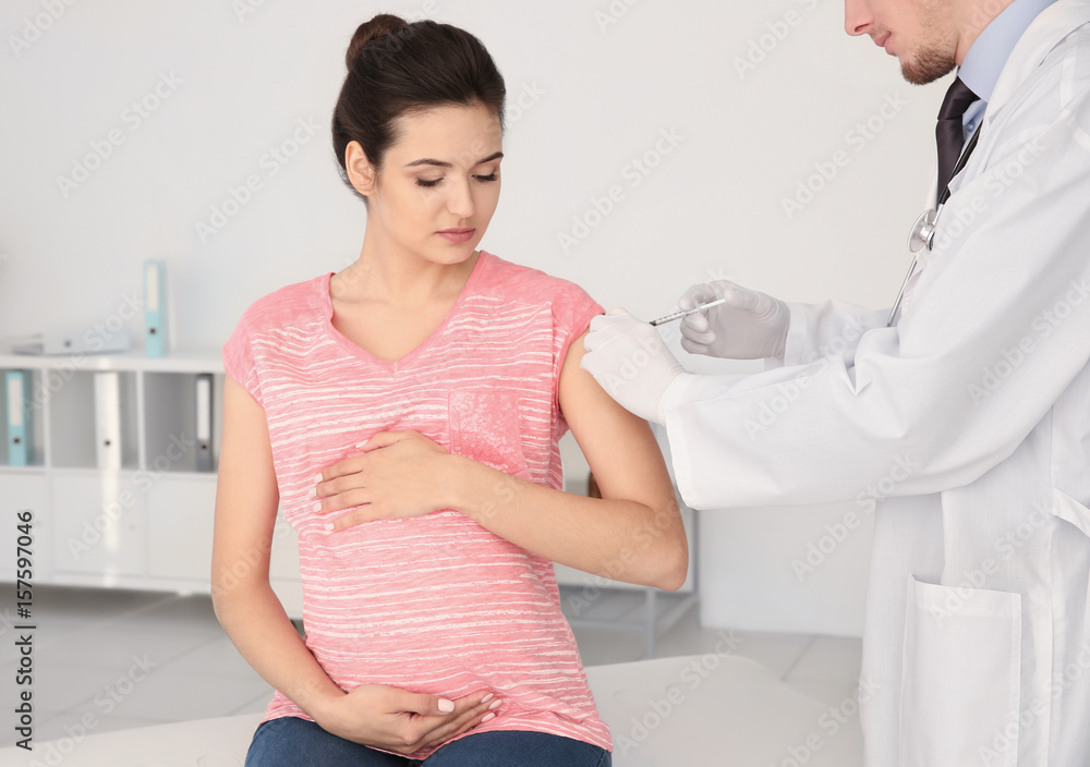 Young pregnant woman receiving injection from medical assistant in clinic Young pregnant woman receiving injection from medical assistant in clinic