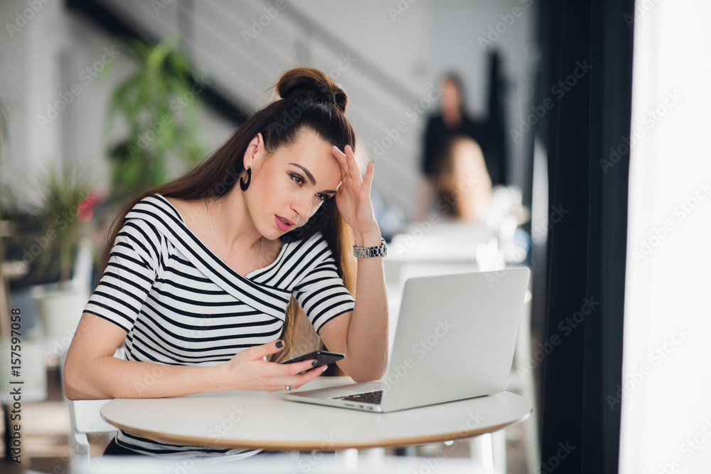 Fototapeta premium Pensive talented attractive female journalist is thinking over creative solutions for making article working in cafe, charming skilled designer noting ideas for start up in her smartphone.