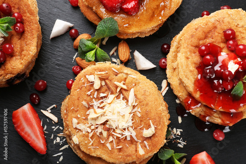 Stacks of delicious coconut pancakes with sweet sauce, berries, shavings and mint on slate plate, close up