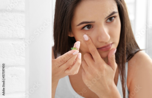 Young woman putting in contact lenses near mirror