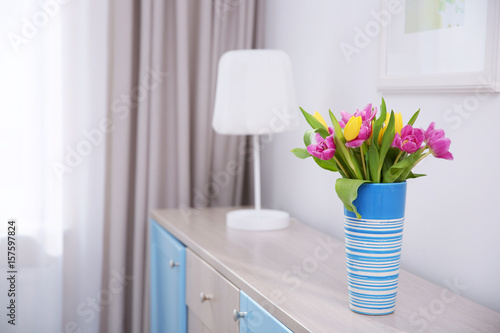 Vase with bouquet of beautiful tulips on chest of drawers