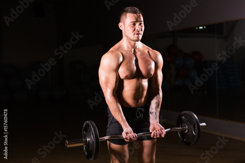 Muscular man working out in gym doing exercises with barbell, strong male naked torso abs.