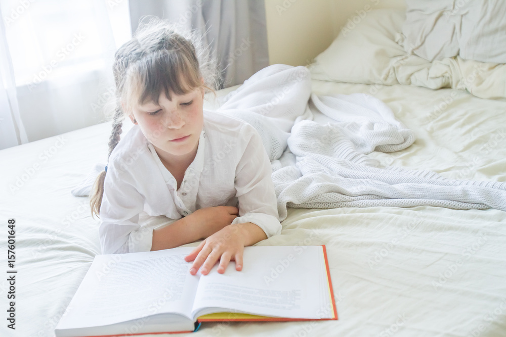 indoor portrait of young european girl lying in bed and reading a book indoor portrait of young european girl lying in bed and reading a book