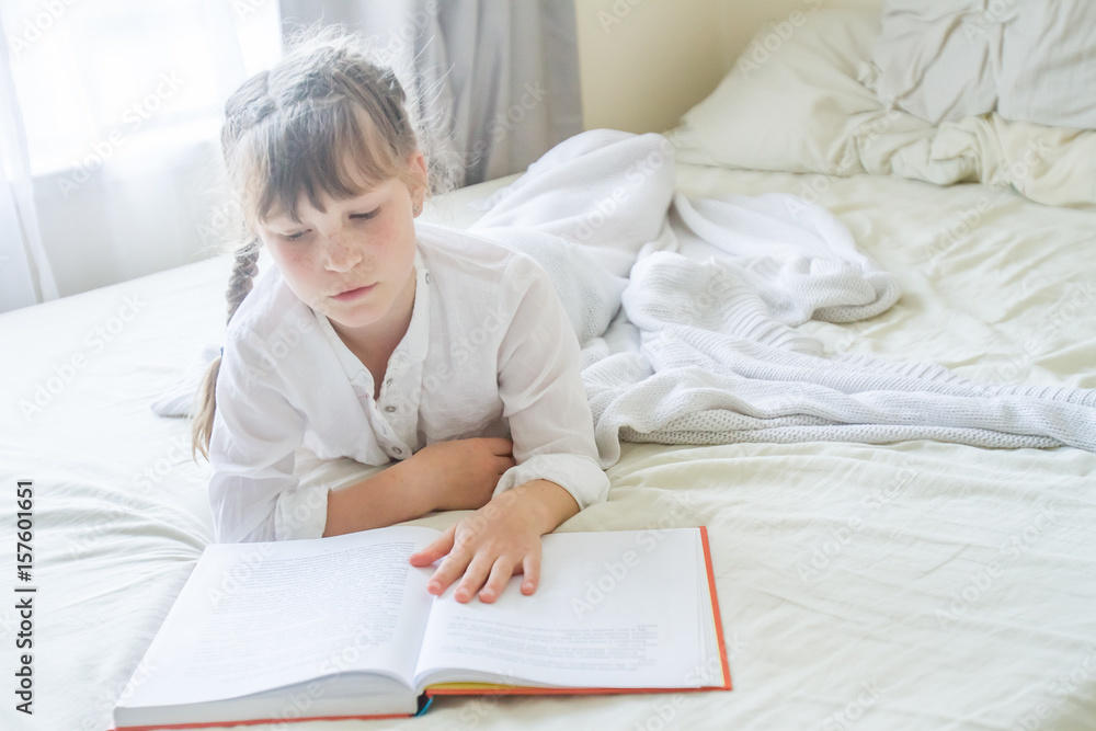 indoor portrait of young european girl lying in bed and reading a book indoor portrait of young european girl lying in bed and reading a book