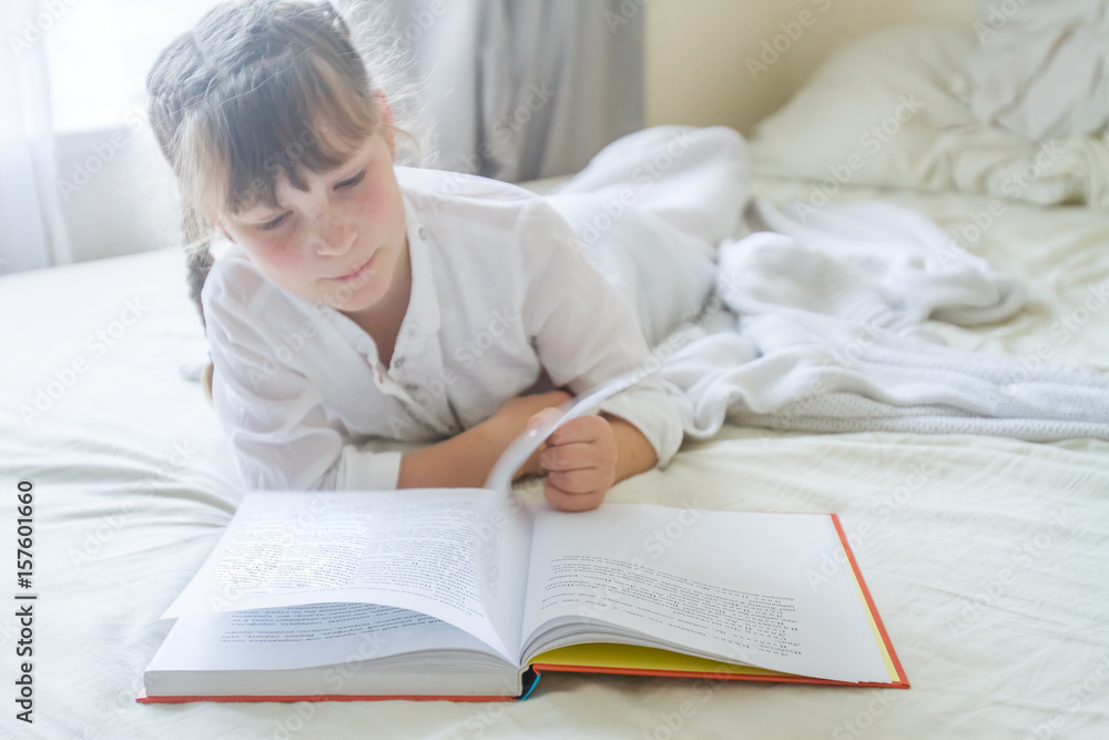 indoor portrait of young european girl lying in bed and reading a book indoor portrait of young european girl lying in bed and reading a book