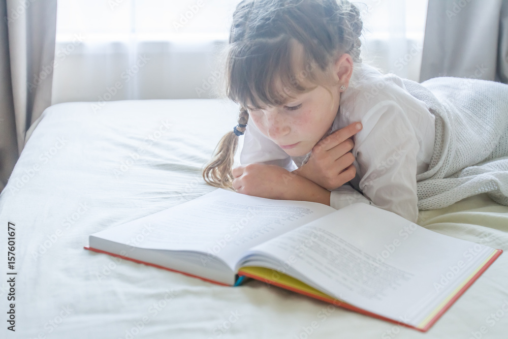 indoor portrait of young european girl lying in bed and reading a book