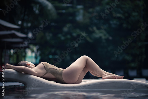 Fototapeta Beautiful lonely girl lies on a lounger in a swimsuit in the pool in tropics of Malaysia