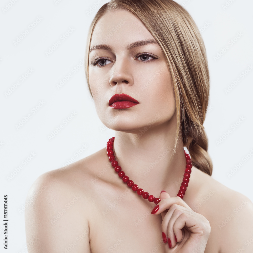 A model with blond hair braided in a braid, fair skin, bare shoulders and a red necklace on the neck.
