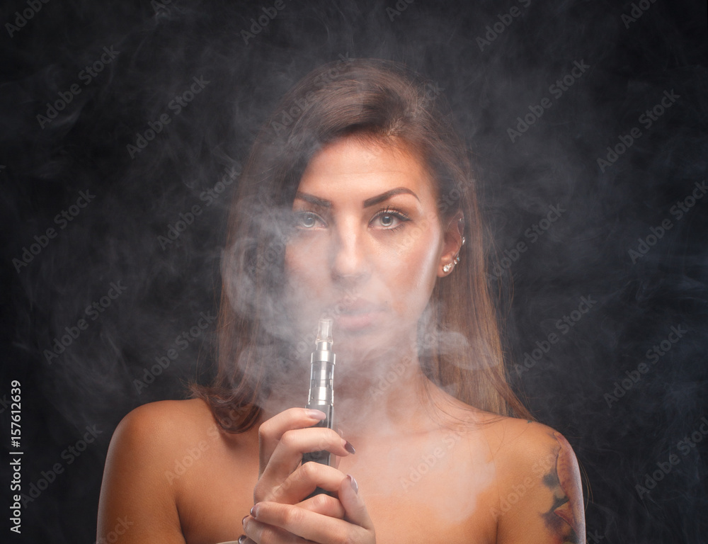 Fototapeta premium Young beautiful woman smoking ( vaping ) e-cigarette. A cloud of vapor.