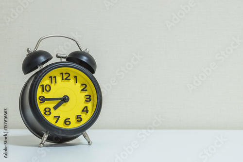 Closeup yellow and black alarm clock for decorate show a quarter to eight o'clock or 7:45 a.m. on white wood desk and cream wallpaper textured background tone with copy space
