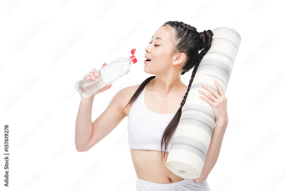 Attractive young asian woman holding yoga mat and drinking water from bottle Attractive young asian woman holding yoga mat and drinking water from bottle