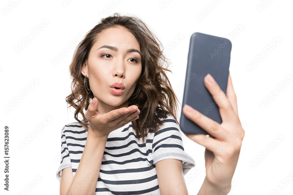 woman blowing kiss while taking selfie on smartphone isolated on white