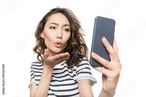 woman blowing kiss while taking selfie on smartphone isolated on white