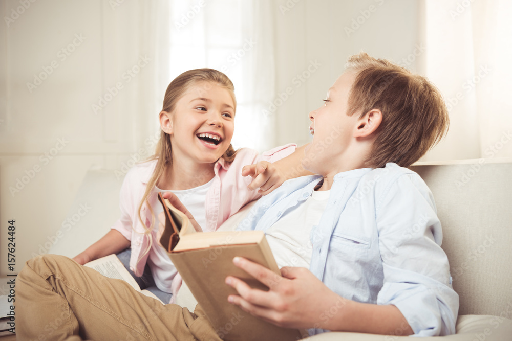 cheerful sister and brother reading book and laughing together at home cheerful sister and brother reading book and laughing together at home