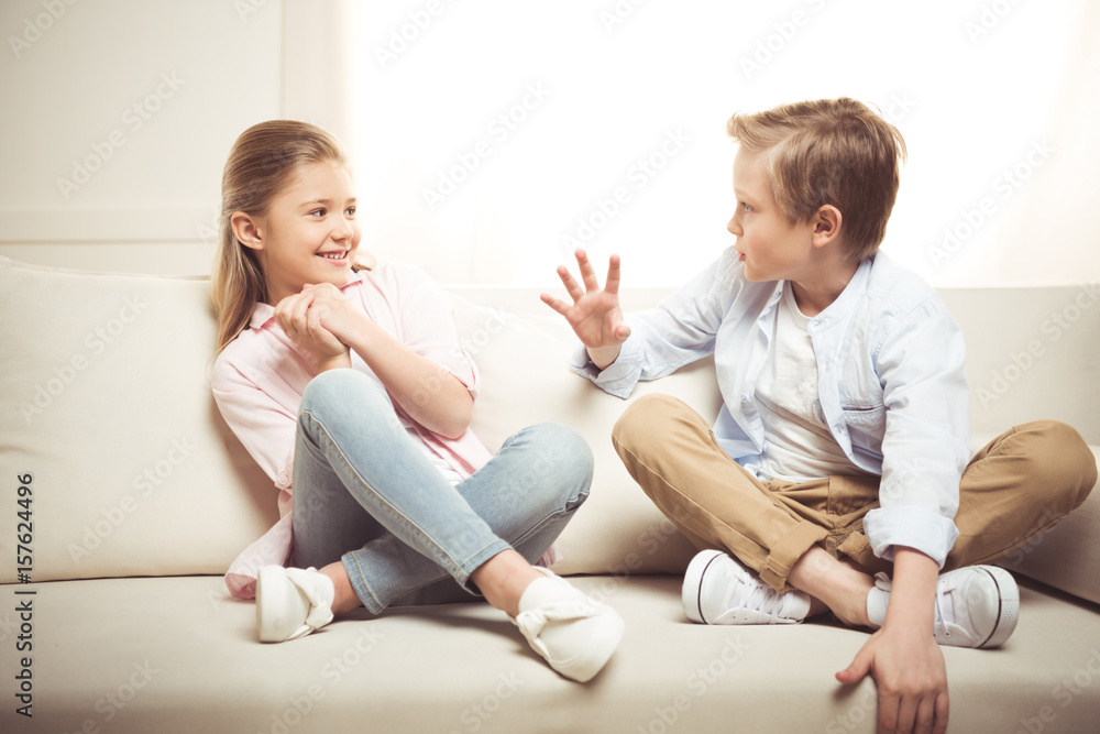 cheerful sister and brother talking together while sitting on sofa at home cheerful sister and brother talking together while sitting on sofa at home