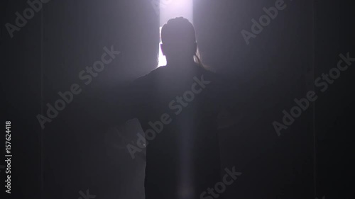 Man silhouette back going to the light at night. Male silhouette going to bright light. Man silhouette walking to light in the darkness. Man open door light in dark. Escape concept