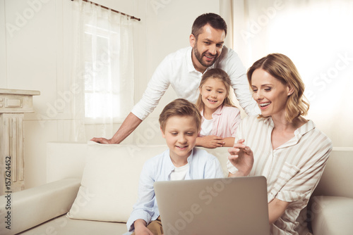 Happy family with two adorable children sitting together and using laptop at home