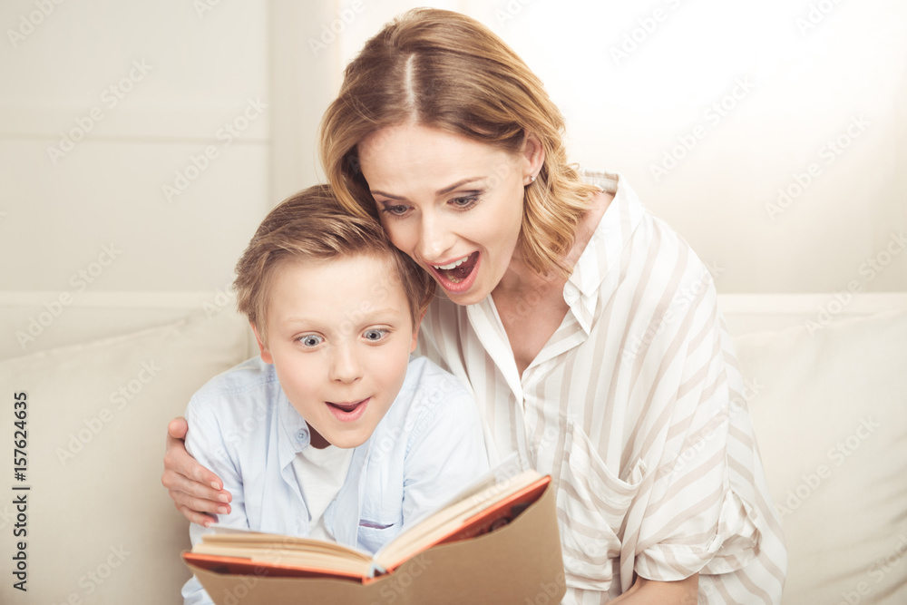Excited mother and son sitting embracing and reading book together Excited mother and son sitting embracing and reading book together