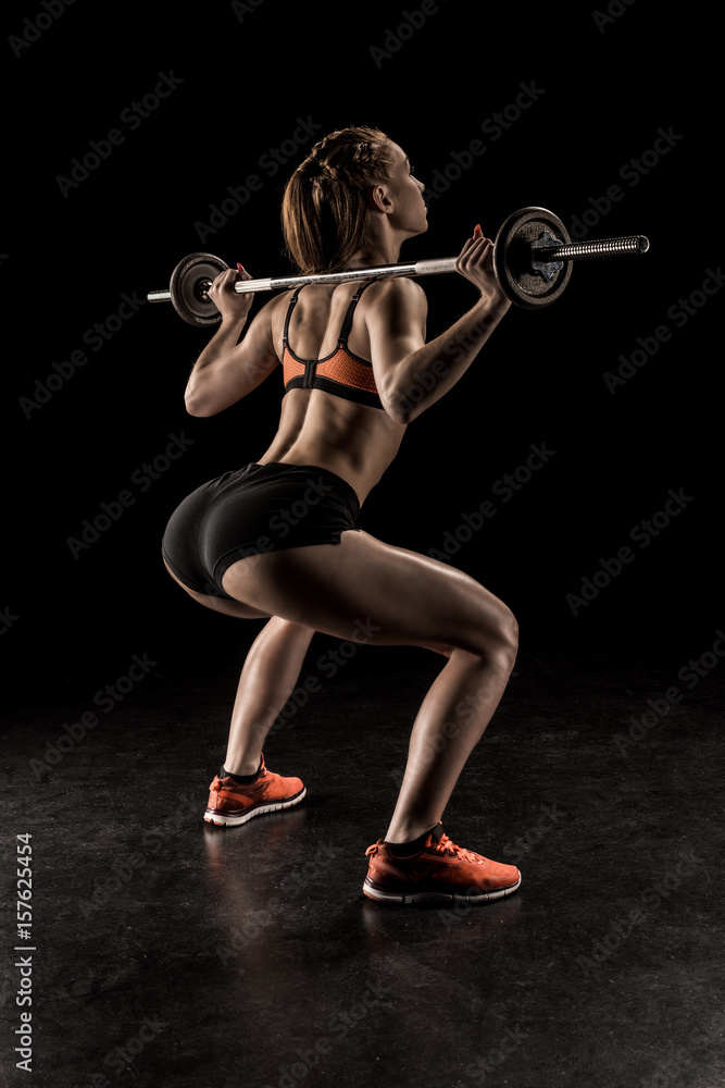 Muscular young woman in sportswear lifting barbell and looking away Muscular young woman in sportswear lifting barbell and looking away