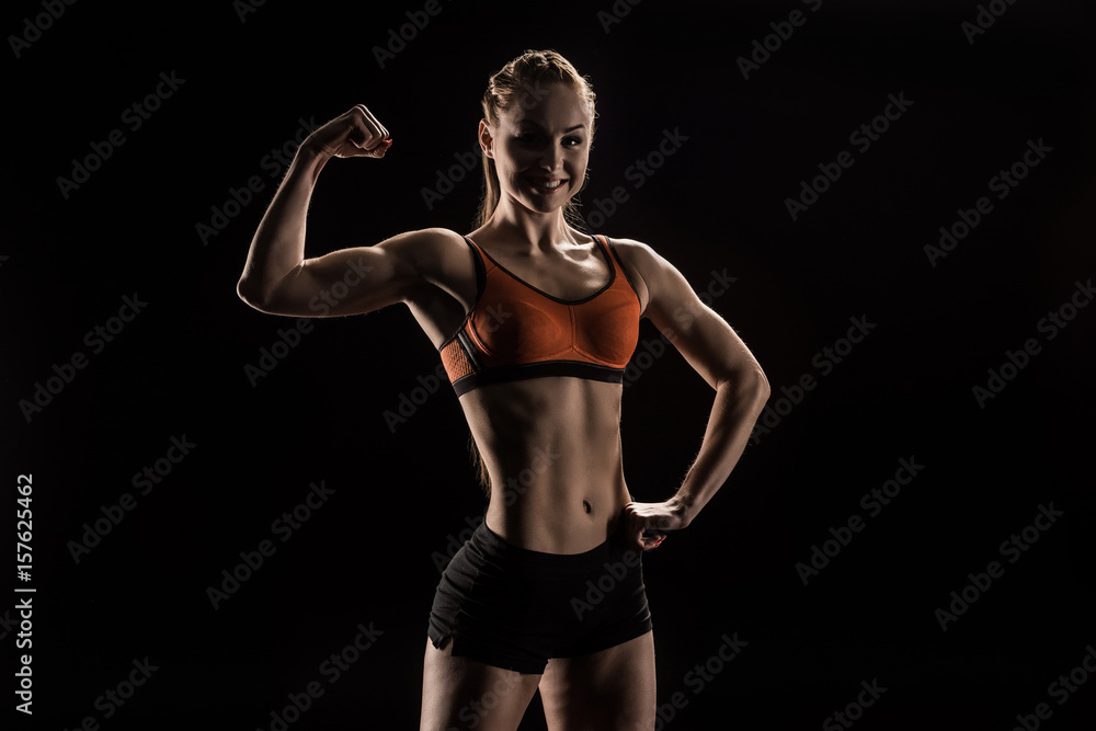 young smiling sportswoman flexing biceps and looking at camera