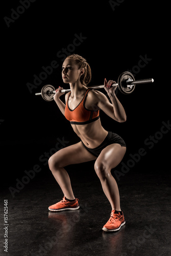 Muscular young sportswoman lifting barbell and looking away