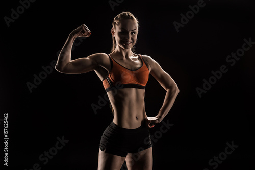 young smiling sportswoman flexing biceps and looking at camera