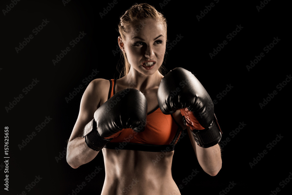 Close-up view of aggressive young sportswoman boxing  in boxing gloves isolated on black