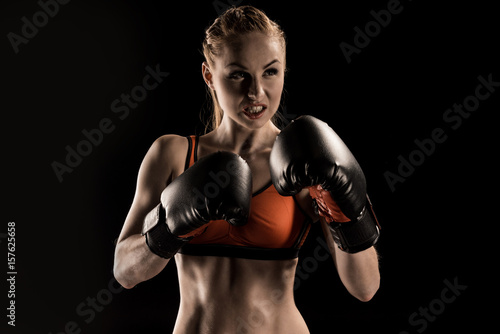 Close-up view of aggressive young sportswoman boxing  in boxing gloves isolated on black © LIGHTFIELD STUDIOS
