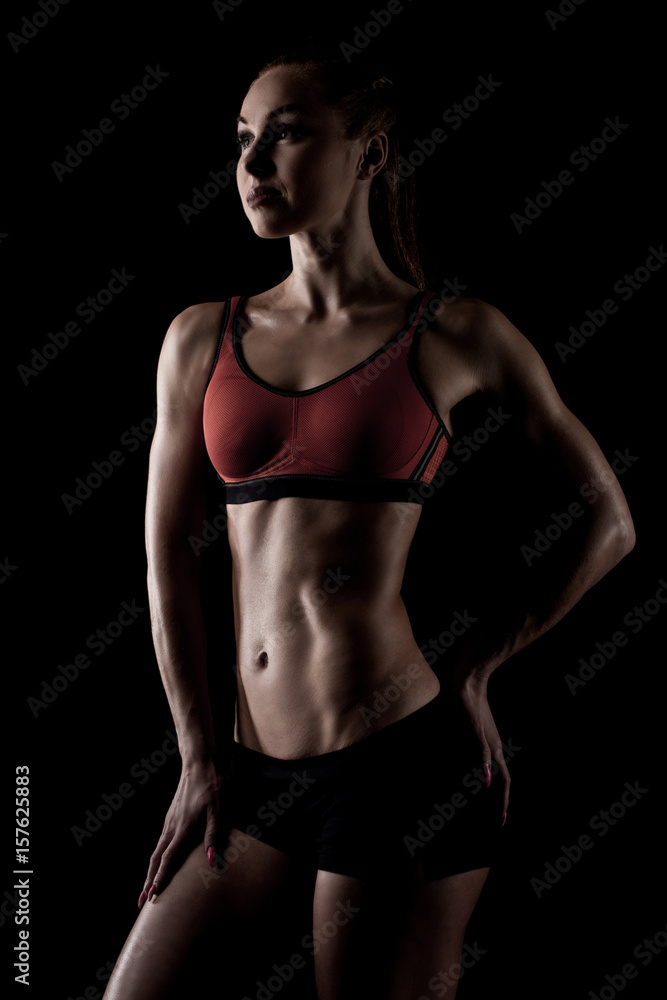 muscular sportswoman posing in sportswear and showing her slim body isolated on black