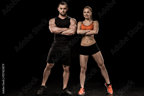 sportive man and woman posing together and looking at camera isolated on black