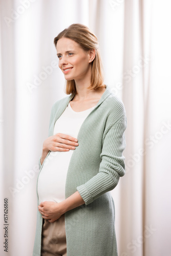 young caucasian pregnant woman smiling and holding stomach