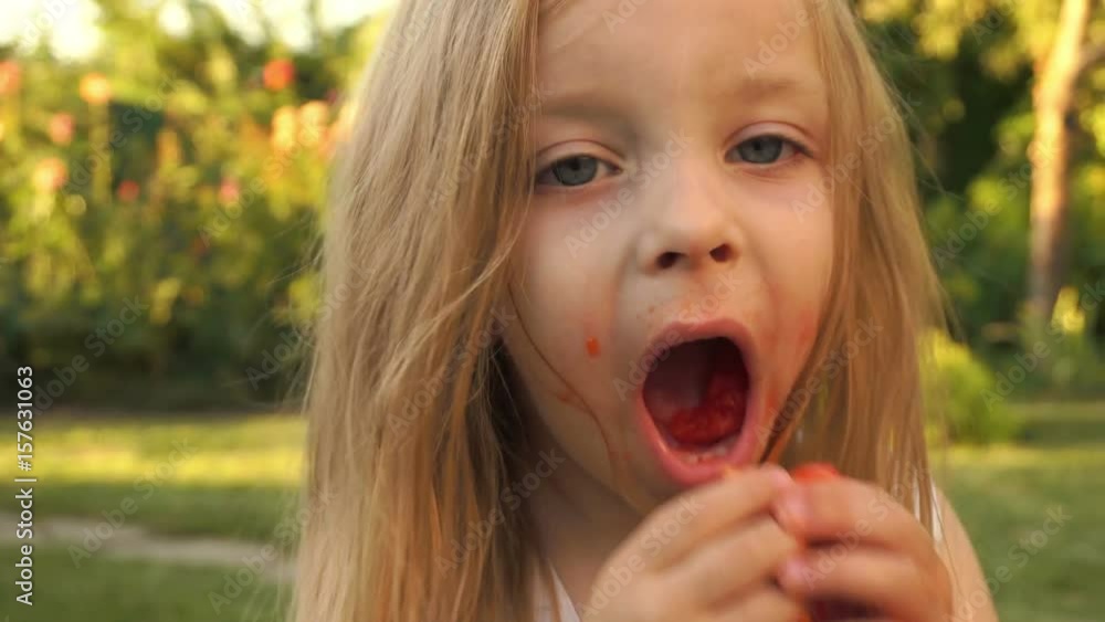 Little sweet girl with pleasure eating a tomato. The face and hands are soiled in tomato juice. Rural life. Ecologically clean food. Little sweet girl with pleasure eating a tomato. The face and hands are soiled in tomato juice. Rural life. Ecologically clean food.
