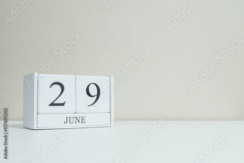 Closeup white wooden calendar with black 29 june word on blurred white wood desk and cream color wallpaper in room textured background with copy space in selective focus at the calendar