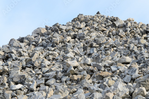 Pile of gray gravel stones with blue sky and clouds background