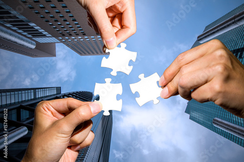 фотографія three hands holding piece of jigsaw puzzle on cityscape background