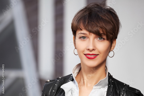 Happy young fashion woman in leather jacket walking in city street