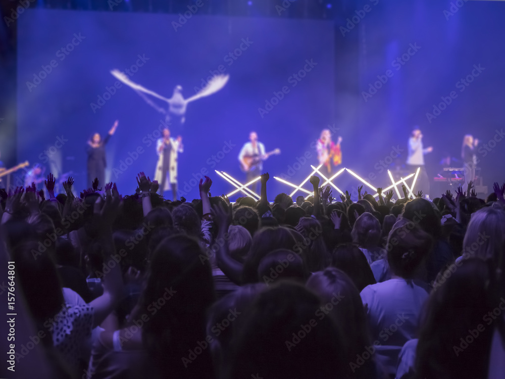 Silhouette of people with hands raised worshiping to the God in concert.