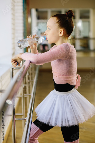 Girl ballet dancer drinking water in ballet class