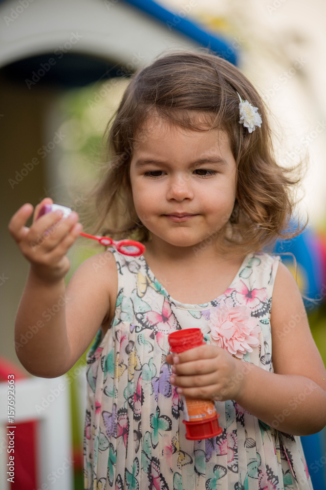 Cute little girl plays with soap bubbles in the garden playground at sunny day Cute little girl plays with soap bubbles in the garden playground at sunny day