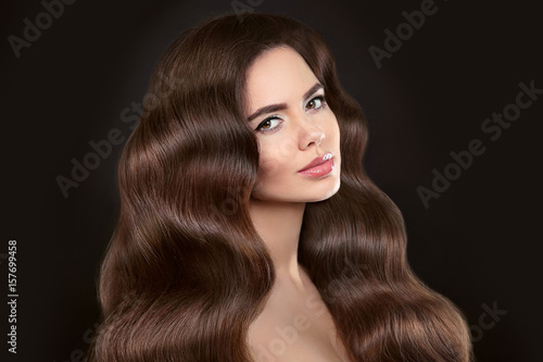 Healthy Hair. Beautiful model girl with shiny brown wavy long hairstyle and makeup isolated on black background. Glossy natural hair. Care and hair products.