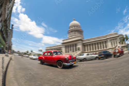 Old classic American cars serving as taxis pass on the main street in front of the Capitolio building in Central Havana, Cuba