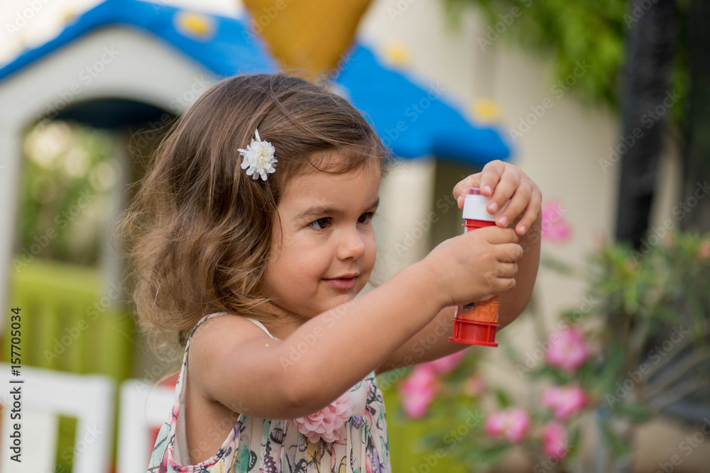 Cute little girl plays with soap bubbles in the garden playground at sunny day Cute little girl plays with soap bubbles in the garden playground at sunny day
