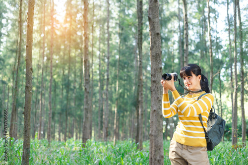 Young Woman in yellow sweater take a photo between travel in pine forest.