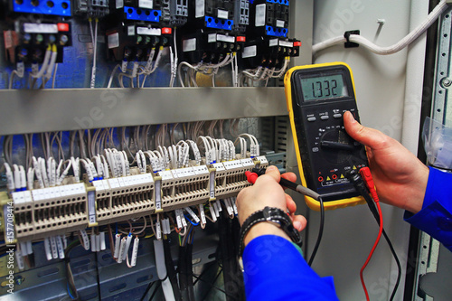 engineer tests industrial electrical circuits with a multimeter in the control terminal box photo