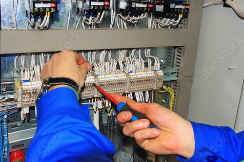 Macro electrician's hands with screwdriver connect wires on background of electrical cabinet