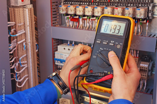 Obraz na płótnie Multimeter in the hands of an electrician close-up on a blurred background of electrical elements w salonie