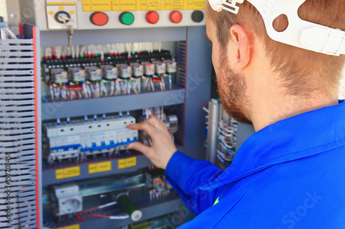 Electrical engineer performs switching of industrial equipment on a blurred background of the control cabinet